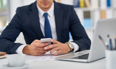 Imagem de um homem de terno sentado em uma cadeira, de frente para uma mesa de escritório branca com um notebook em cima.