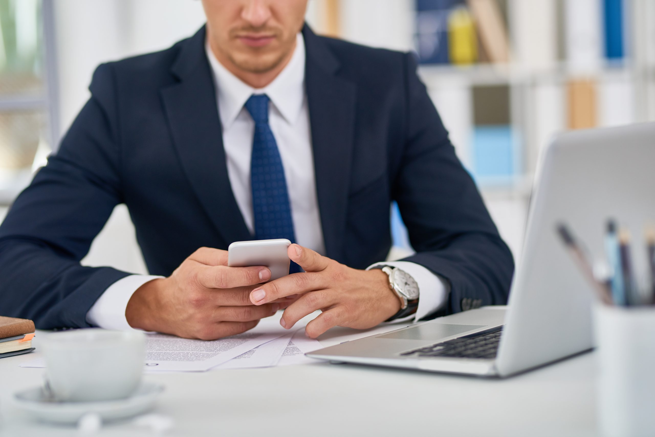 Imagem de um homem de terno sentado em uma cadeira, de frente para uma mesa de escritório branca com um notebook em cima.